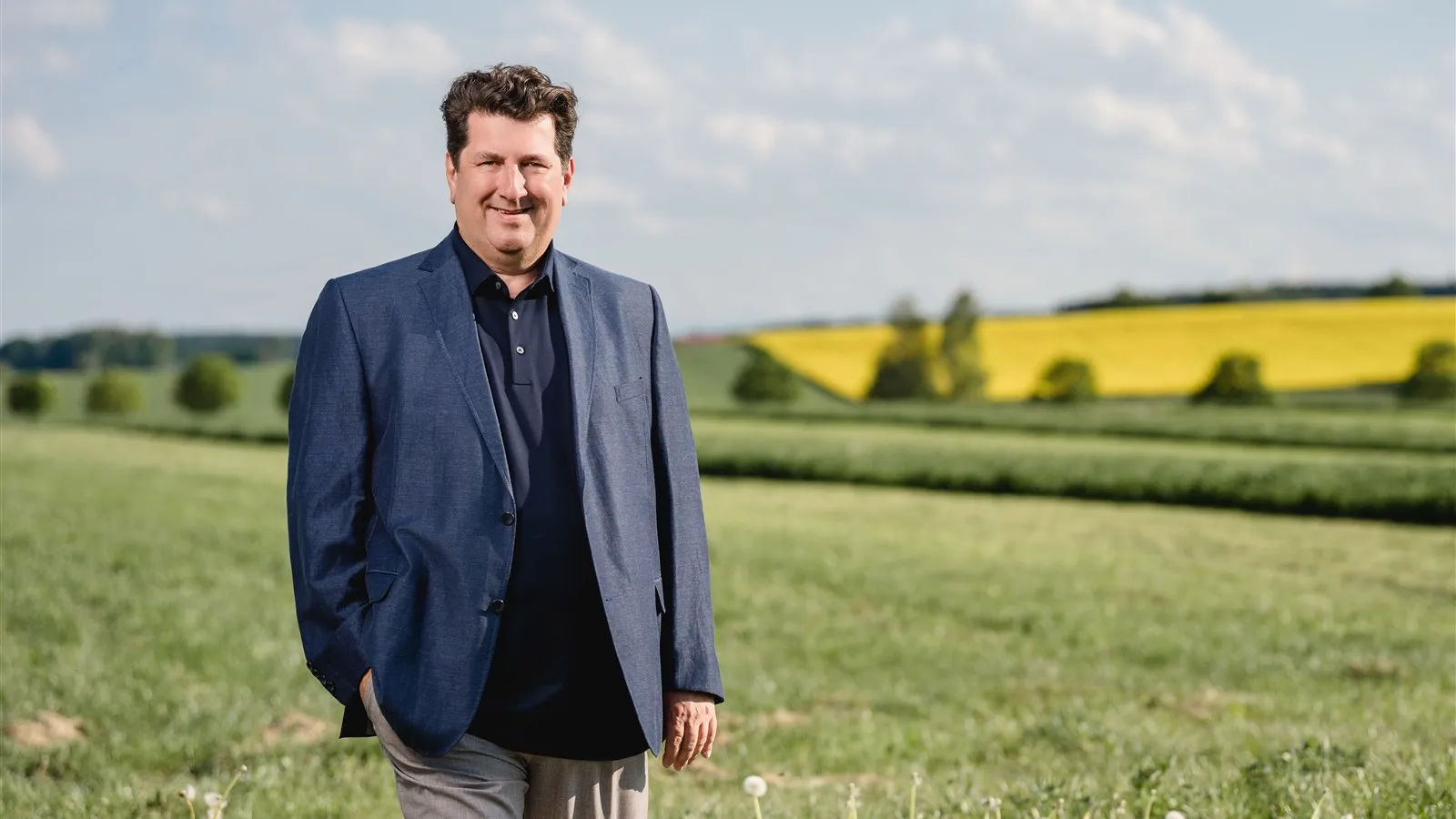 Alexander Köhler auf einer Wiese, im Hintergrund ein Rapsfeld